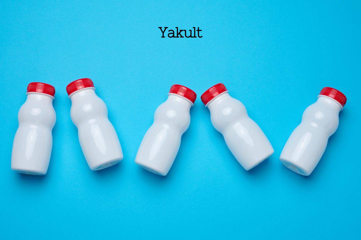 Five unlabeled white bottles with red tops representing Yakult.