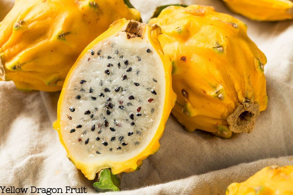 Yellow dragon fruit cut open to reveal white flesh and black seeds on a burlap backdrop.