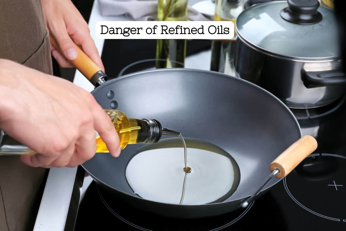 A hand pouring an unmarked bottle of yellow cooking oil into a wok on a stove top.