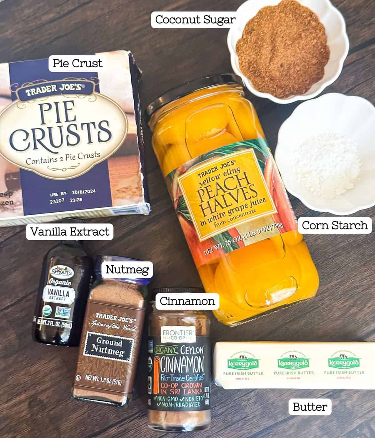 Ingredients for peach cobbler laid out on a wooden table, featuring pie crusts, canned peaches, and spices.