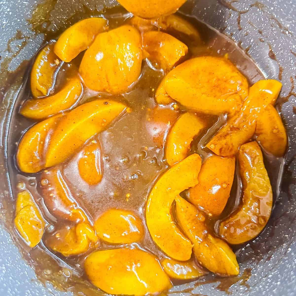 Bright, sliced peaches in a saucepan coated with a glossy, cinnamon-infused sauce.