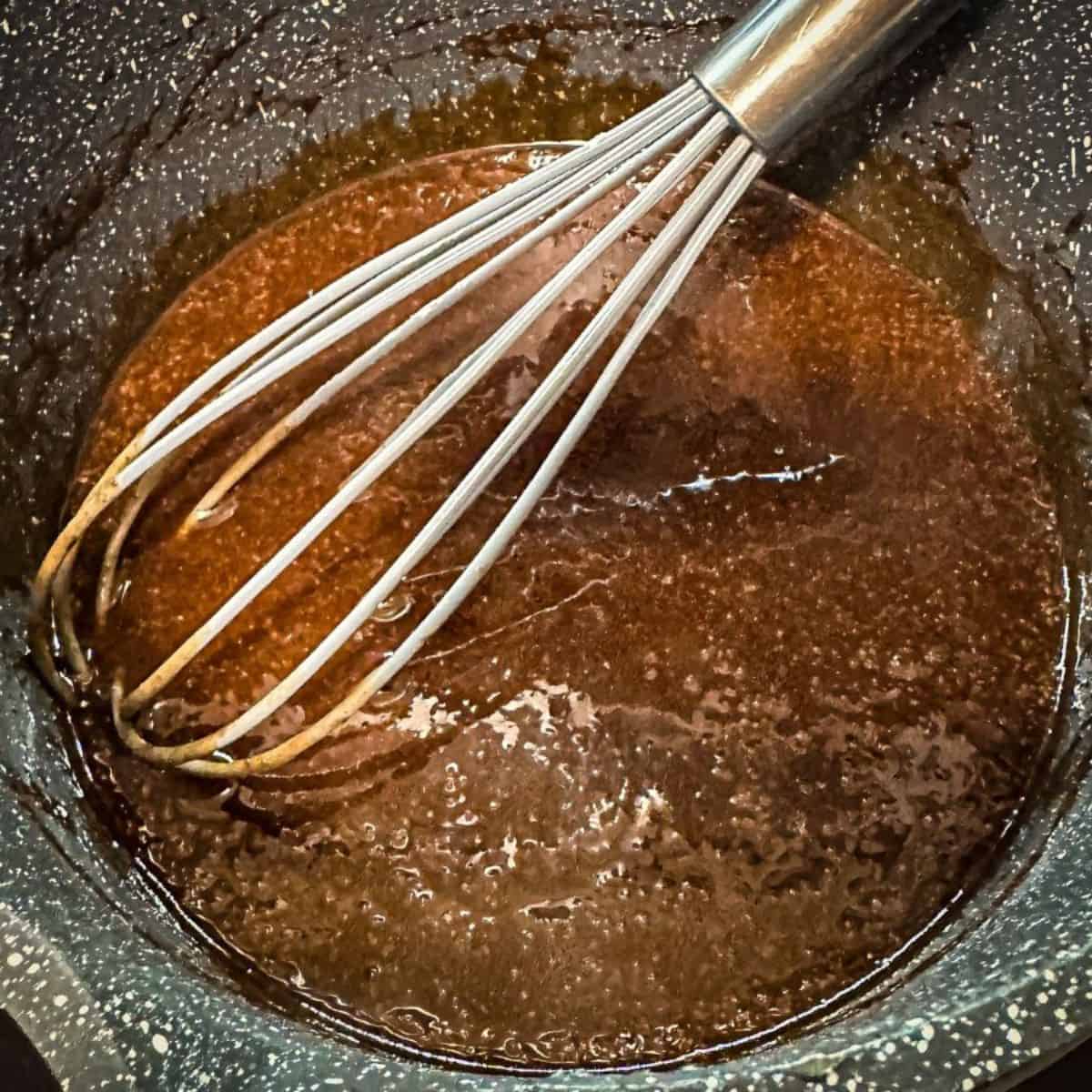 A whisk mixing brown sauce in a pot, preparing the spiced base for peach cobbler.