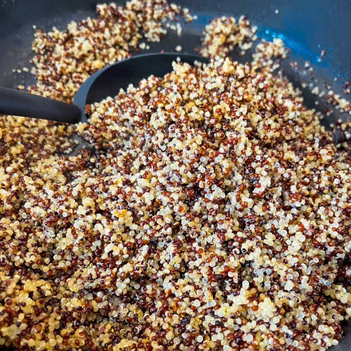 A skillet full of tri-colored quinoa cooked being stirred by a black spoon.