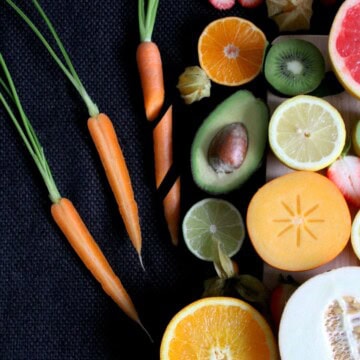 A variety of whole fruits and vegetables including carrots, oranges, limes avocado, and melon.