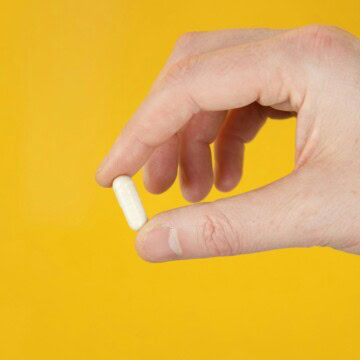 A hand holding a single probiotic capsule.