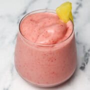A strawberry smoothie in a glass with a pineapple garnish.