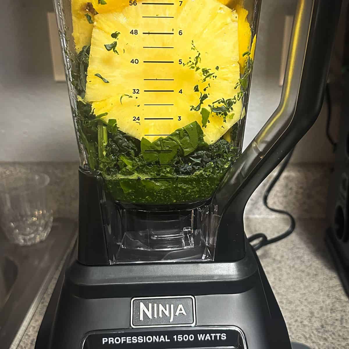 Pineapple, mango, and banana added to broken down greens in a blender.