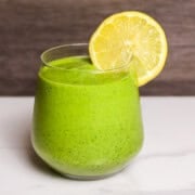 A vibrant green smoothie in a glass with a lemon wheel garnishment.