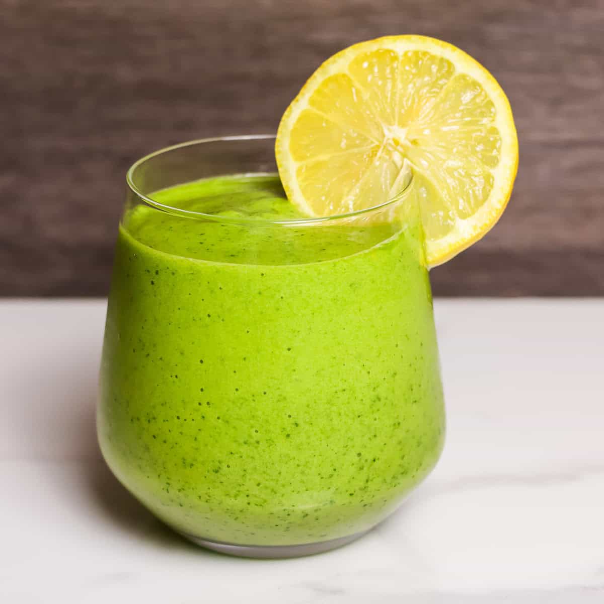 A vibrant green smoothie in a glass with a lemon wheel garnishment.