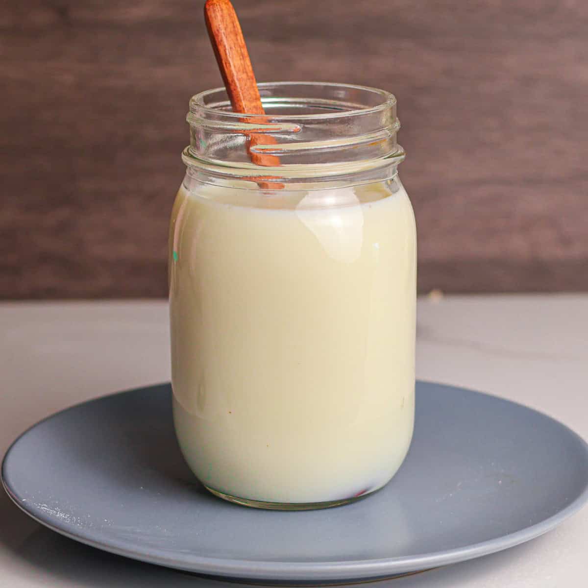 A wooden spoon stirring the raw milk in a jar to make kefir.
