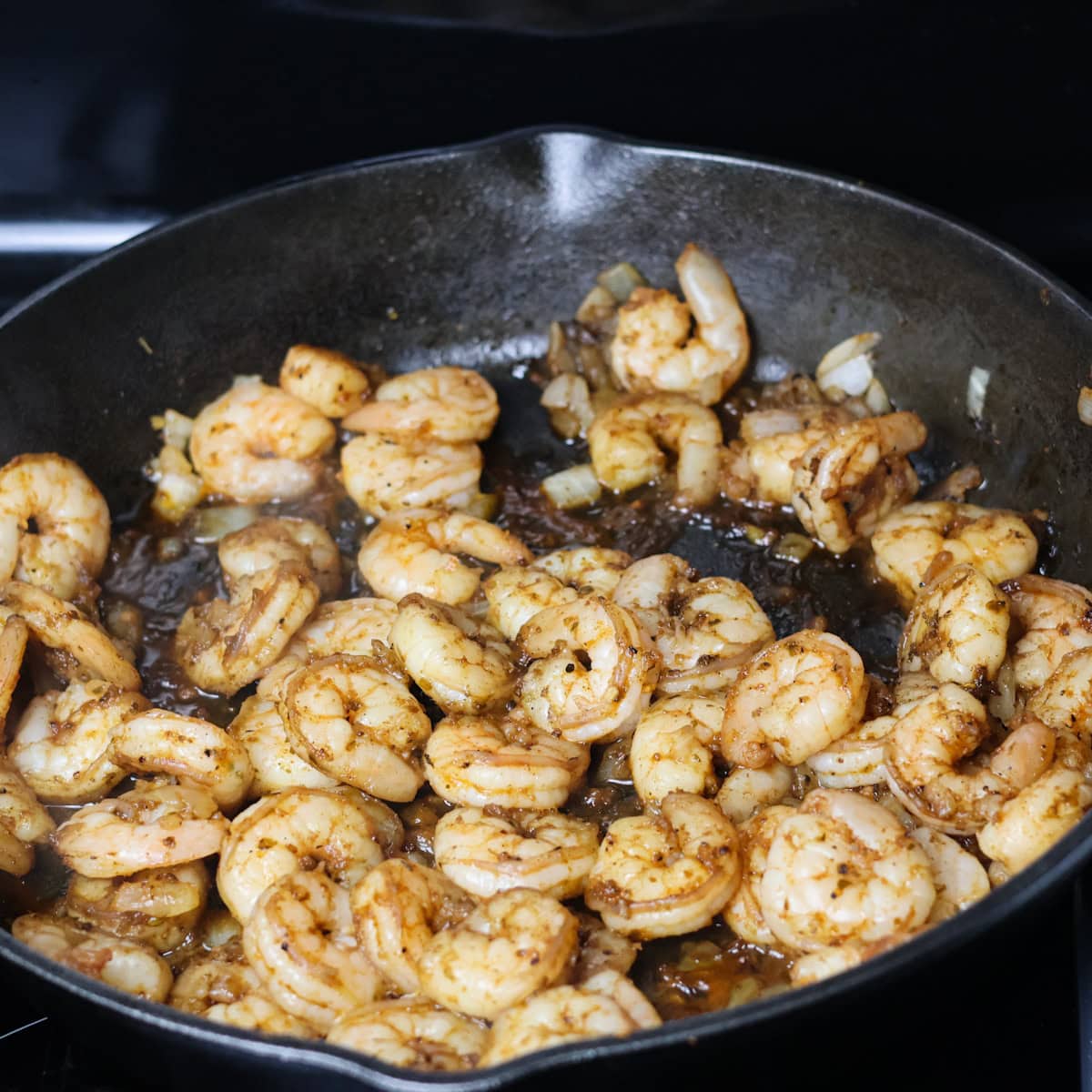 Seasoned Shrimp cooking in a skillet with onions and garlic.
