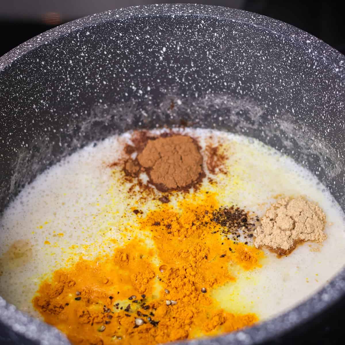 Warming spices and sweetener added to warmed milk in a saucepan.