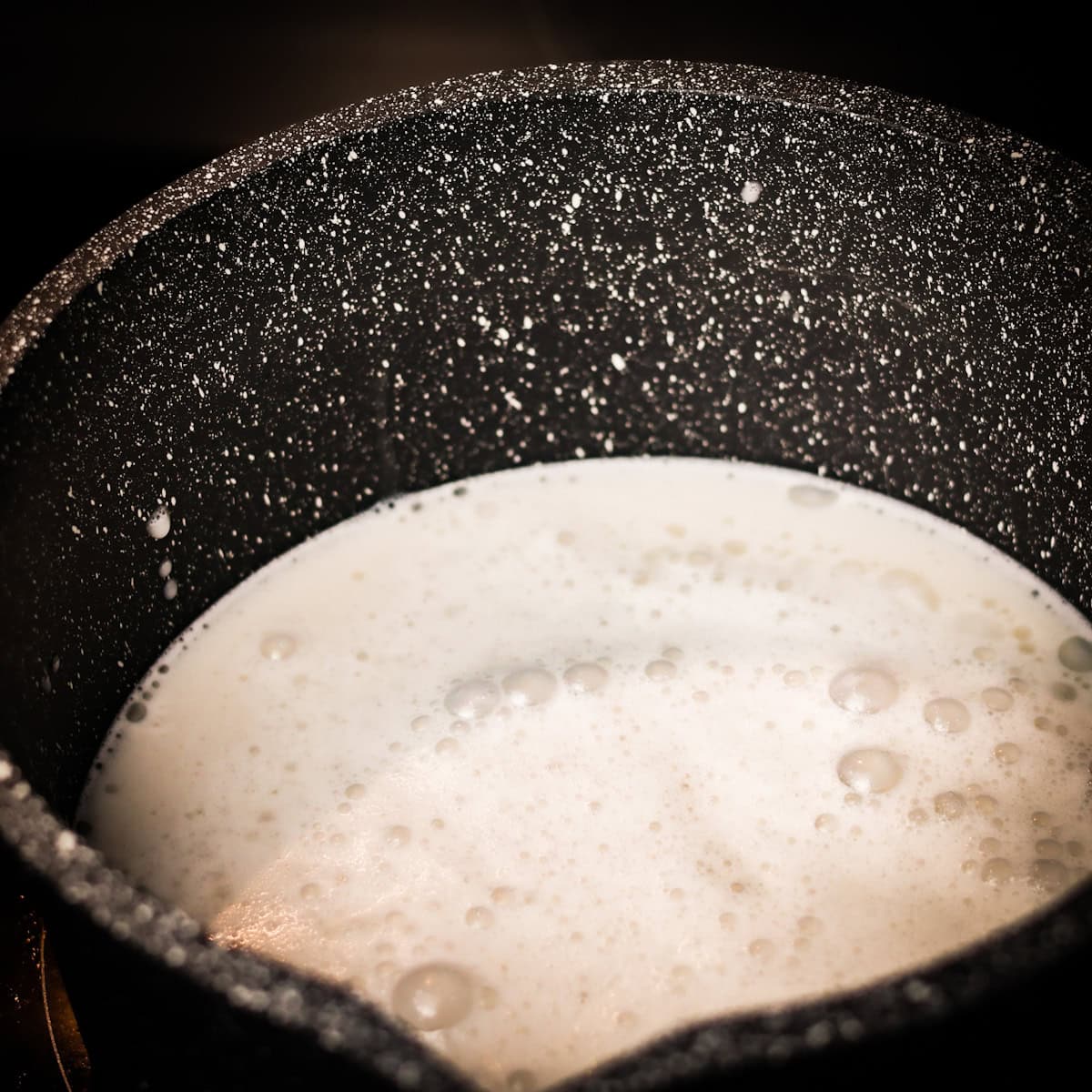 Frothy coconut milk heating on a stovetop.
