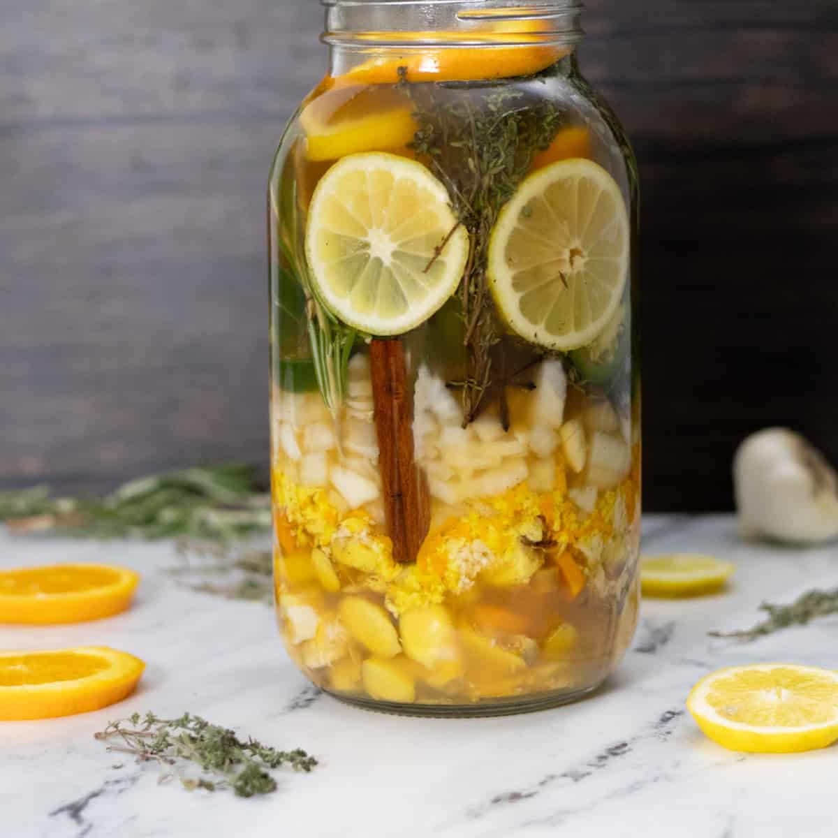 A jar of roots herbs and citrus infusing in vinegar to make fire cider.