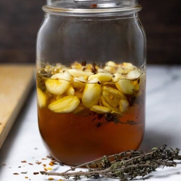 A jar of garlic and honey fermenting with thyme and red pepper flakes.