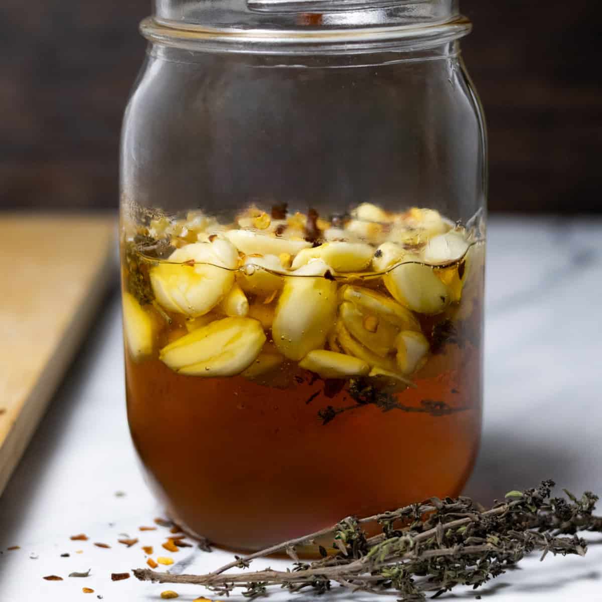 A jar of garlic and honey fermenting with thyme and red pepper flakes.