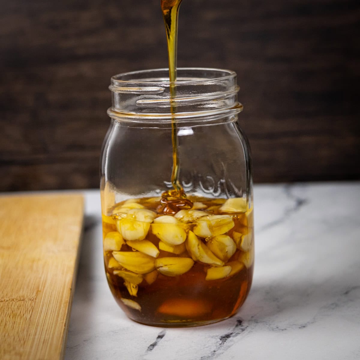 Honey pouring into a jar of garlic cloves.
