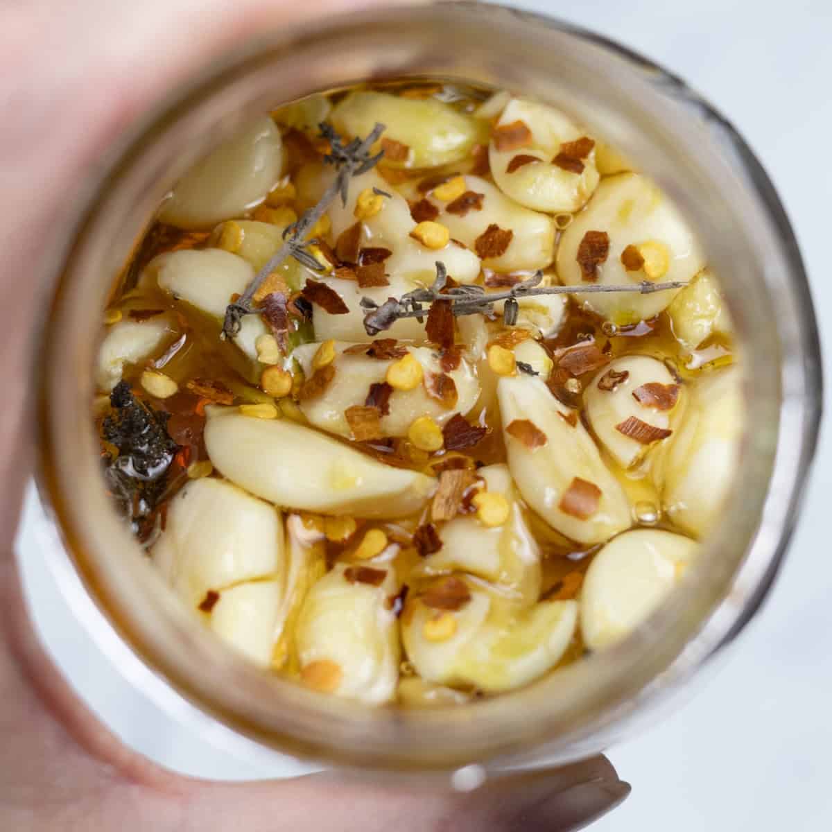 Red pepper flakes and fresh thyme on on top of honey and garlic in a jar.