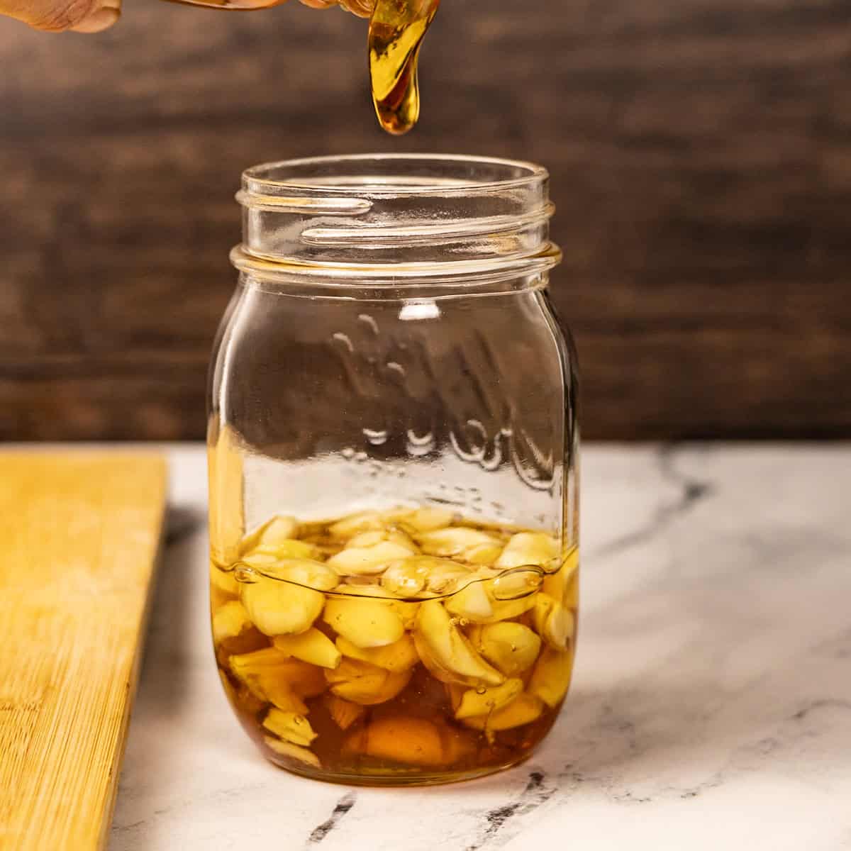 Honey pouring over crushed garlic in a jar.