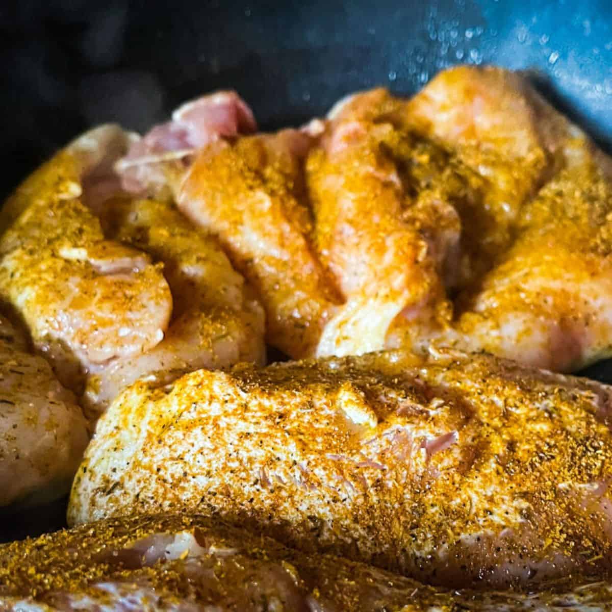 Chicken breasts cooking seasoned with jerk seasoning.