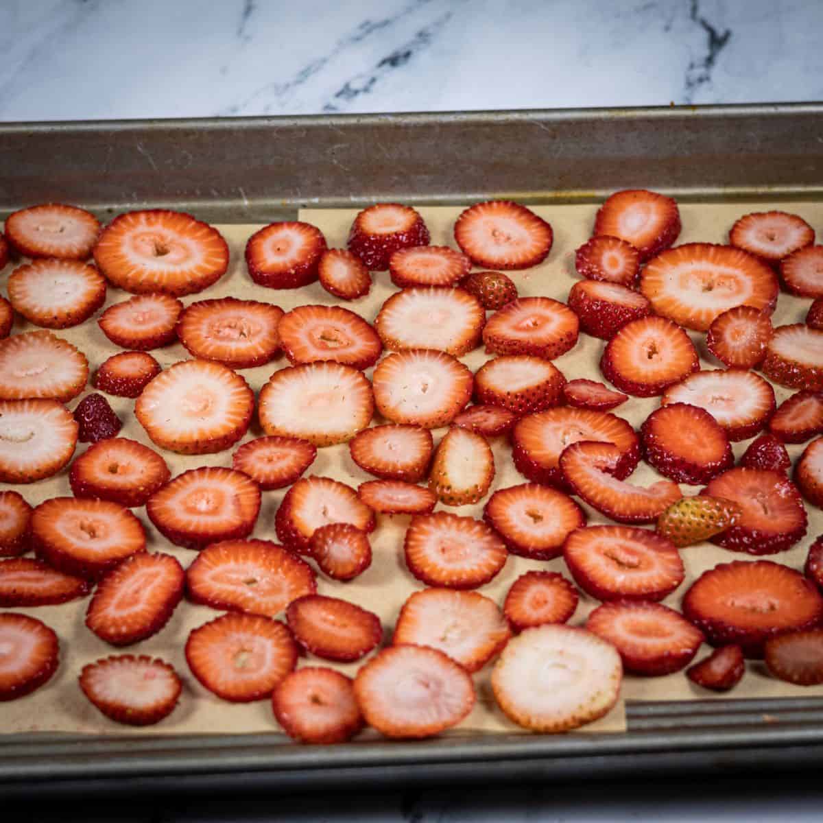 Strawberry slices lined up in an oven layer over a parchment paper lined baking sheet.