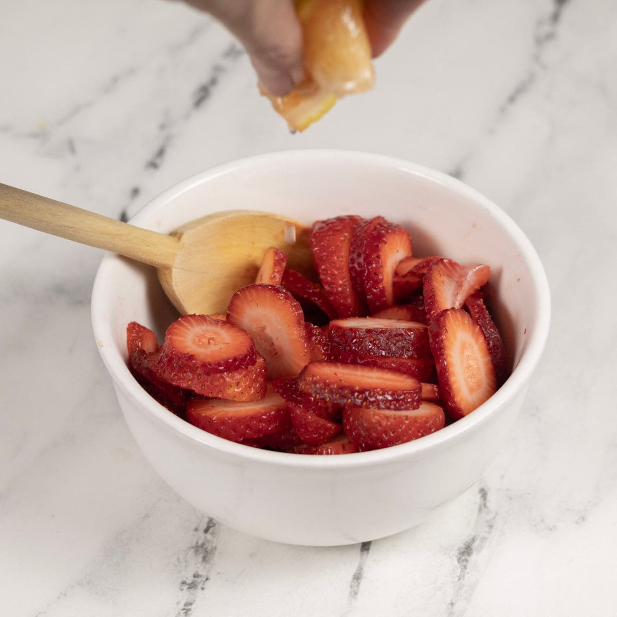 Grapefruit being squeezed over a bowl of sliced strawberries.