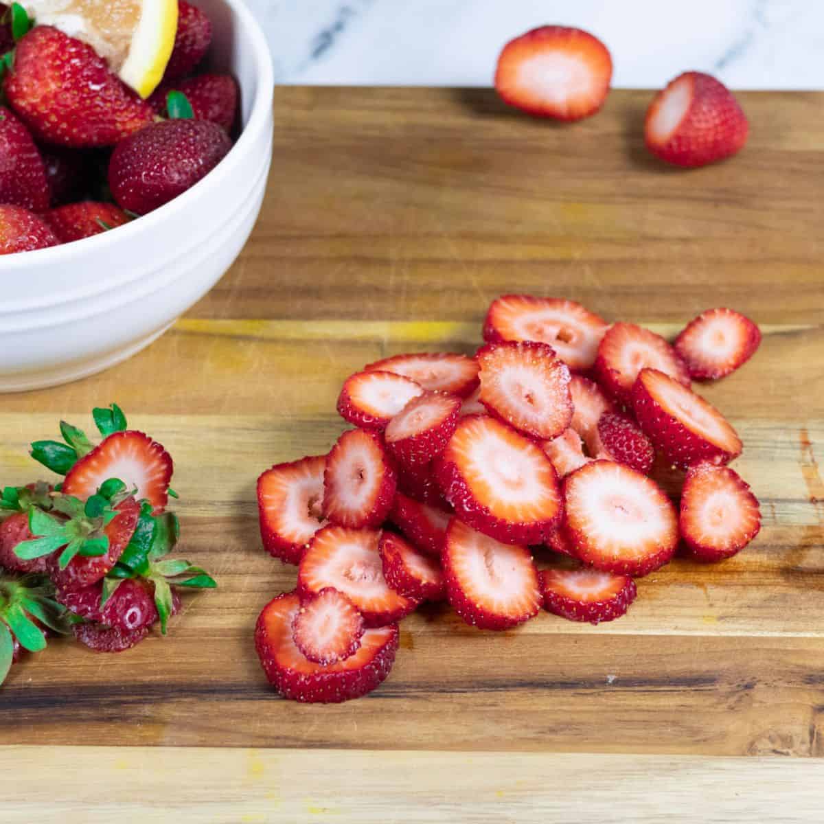Freshly sliced strawberries on a cutting board.